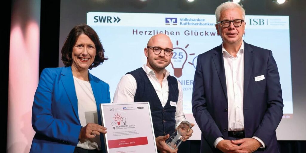 Ron Richter von der klimafarmer GmbH (mi.) bekommt den Preis "Pioniergeist 2023" von der rheinland-pfälzischen Wirtschaftsministerin Daniela Schmitt (li.) und Herbert Kohlberg, Vorstandsmitglied der Volksbank Darmstadt Mainz eG, überreicht. Foto: ISB/Alexander Sell.